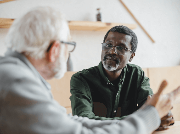 Image of two men and one boy sitting at the edge of a river fishing